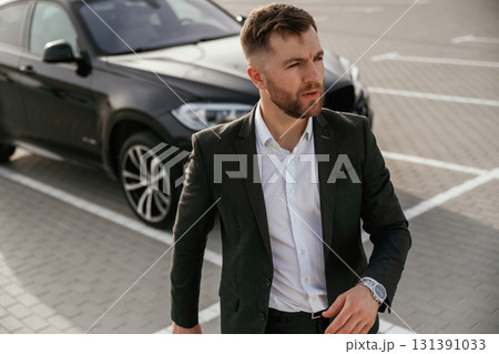Businessman in suit is near his black car outdoors 131391033