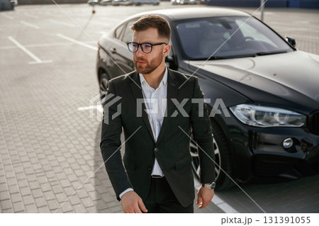 Handsome smart guy in glasses. Businessman in suit is near his black car outdoors 131391055