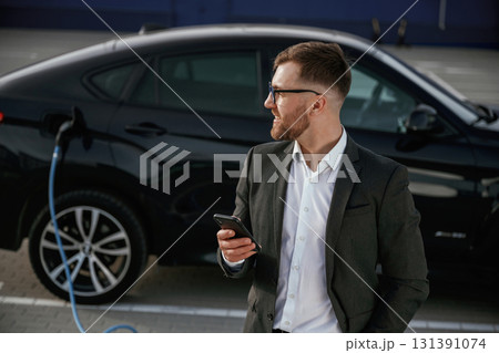 Smartphone in hand. Businessman in suit is near his black car outdoors 131391074