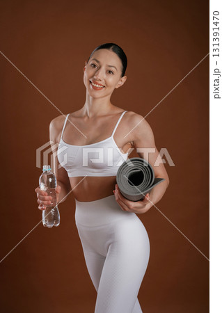 Fresh water in bottle and yoga mat. Beautiful fitness woman is in the studio Fresh water in bottle and yoga mat. Beautiful fitness woman is in the studio 131391470
