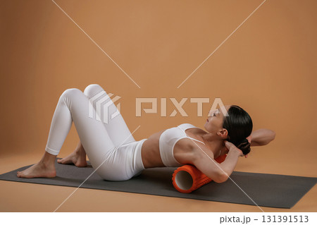 Using roll on the yoga mat. Beautiful fitness woman is in the studio 131391513