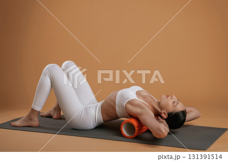 Using roll on the yoga mat. Beautiful fitness woman is in the studio 131391514