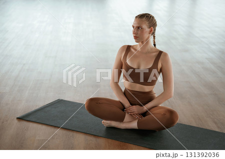 Sitting on yoga mat, taking a break. Fitness woman in sportswear is indoors Sitting on yoga mat, taking a break. Fitness woman in sportswear is indoors 131392036