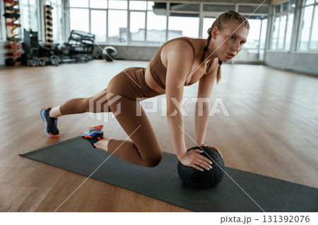 Using fitness ball on yoga mat. Woman in sportswear is indoors Using fitness ball on yoga mat. Woman in sportswear is indoors 131392076
