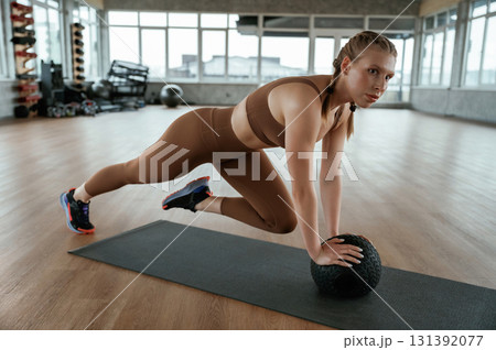 Using fitness ball on yoga mat. Woman in sportswear is indoors 131392077