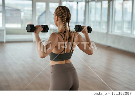 With dumbbells in hands. Fitness woman in sportswear is indoors 131392097