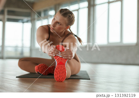 On the floor, doing stretching. Fitness woman in sportswear is indoors 131392119