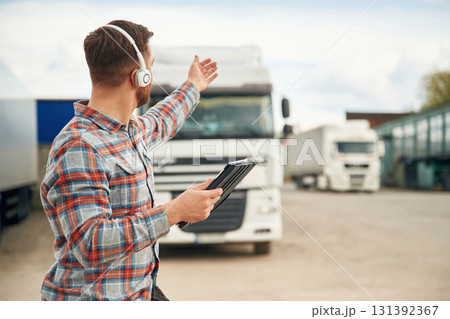 Showing the way, with tablet. Man is standing against trucks outdoors Showing the way, with tablet. Man is standing against trucks outdoors 131392367