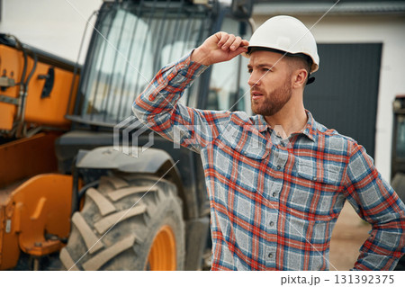 In white hard hat. Man is with tractor. Agricultural worker In white hard hat. Man is with tractor. Agricultural worker 131392375
