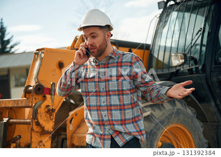 Talking by phone. Man is with tractor. Agricultural worker Talking by phone. Man is with tractor. Agricultural worker 131392384