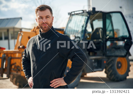 In black hoodie. Standing and posing. Man is with tractor. Agricultural worker In black hoodie. Standing and posing. Man is with tractor. Agricultural worker 131392421