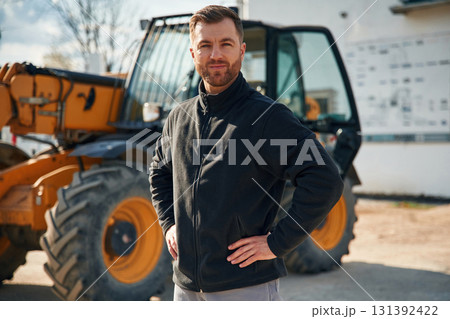 In black hoodie. Standing and posing. Man is with tractor. Agricultural worker In black hoodie. Standing and posing. Man is with tractor. Agricultural worker 131392422