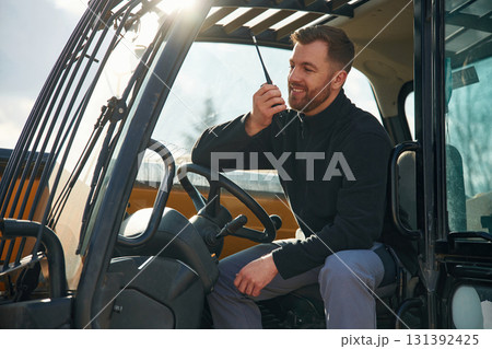 Walkie talkie device, conversation, orders. Man is with tractor. Agricultural worker 131392425