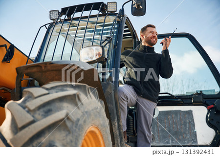 View from below, using walkie talkie. Man is with tractor. Agricultural worker View from below, using walkie talkie. Man is with tractor. Agricultural worker 131392431
