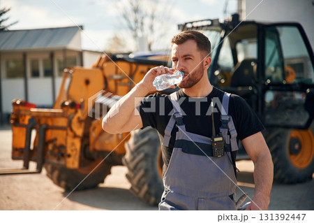 Drinking water, taking a break, tired. Man is with tractor. Agricultural worker Drinking water, taking a break, tired. Man is with tractor. Agricultural worker 131392447