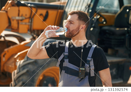 Bottle of water, drinking, taking a break. Man is with tractor. Agricultural worker Bottle of water, drinking, taking a break. Man is with tractor. Agricultural worker 131392574