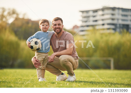 Sitting, holding soccer ball. Happy father with son are having fun on the field at summertime 131393090