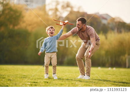 In casual clothes. Running with toy plane. Happy father with son are having fun on the field at summertime 131393123