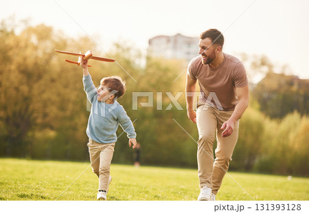 Summertime happiness. Running with toy plane. Father with son are having fun on the field Summertime happiness. Running with toy plane. Father with son are having fun on the field 131393128