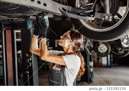 A female mechanic is diligently working underneath a vehicle inside a garage environment A female mechanic is diligently working underneath a vehicle inside a garage environment 131393130