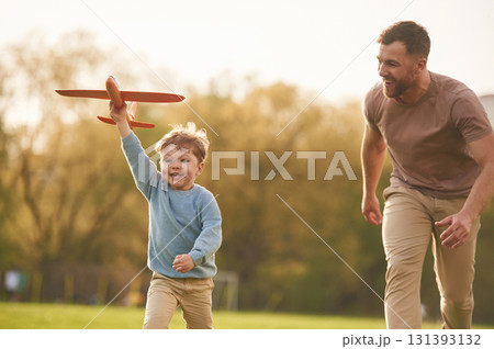 Summertime happiness. Running with toy plane. Father with son are having fun on the field Summertime happiness. Running with toy plane. Father with son are having fun on the field 131393132