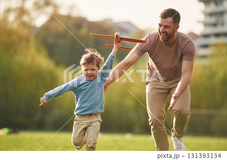Flying high, holding toy plane, running. Happy father with son are having fun on the field at summertime Flying high, holding toy plane, running. Happy father with son are having fun on the field at summertime 131393134