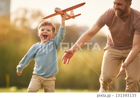 Flying high, holding toy plane, running. Happy father with son are having fun on the field at summertime 131393135