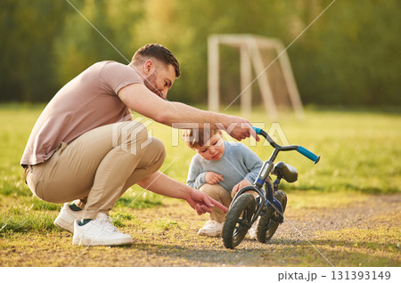 Showing the parts of the bicycle. Happy father with son are having fun on the field at summertime Showing the parts of the bicycle. Happy father with son are having fun on the field at summertime 131393149