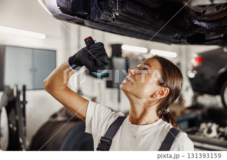 A mechanic is working under a car, utilizing a flashlight in a garage environment during repairs 131393159