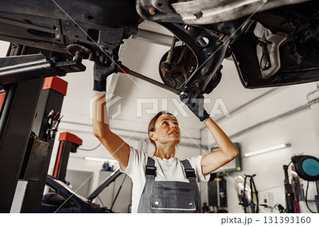A skilled female mechanic works under a vehicle in a busy workshop, showcasing her dedication 131393160