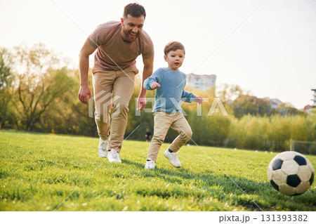 Game of soccer. With ball. Happy father with son are having fun on the field at summertime 131393382