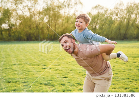 Sitting on man's shoulders. Happy father with son are having fun on the field at summertime Sitting on man's shoulders. Happy father with son are having fun on the field at summertime 131393390