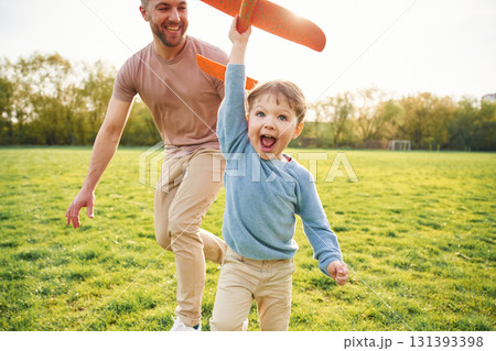 Orange colored toy plane, playing. Happy father with son are having fun on the field at summertime Orange colored toy plane, playing. Happy father with son are having fun on the field at summertime 131393398