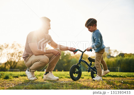 Little bicycle. Happy father with son are having fun on the field at summertime Little bicycle. Happy father with son are having fun on the field at summertime 131393433