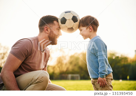 Soccer ball, holding it by heads, fun. Happy father with son are on the field at summertime 131393450
