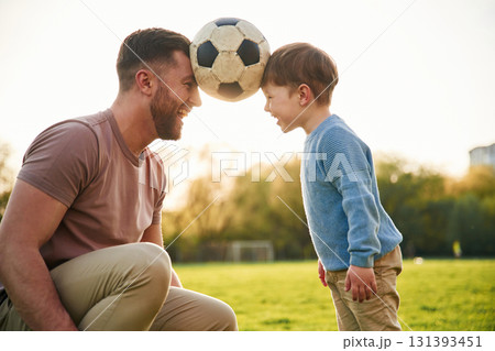 Soccer ball, holding it by heads, fun. Happy father with son are on the field at summertime 131393451