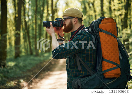 Photographer with camera. Bearded man is in the forest at daytime 131393668