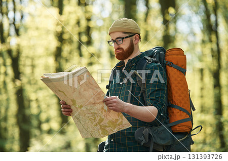 Focused on reading the map. Bearded man is in the forest at daytime Focused on reading the map. Bearded man is in the forest at daytime 131393726