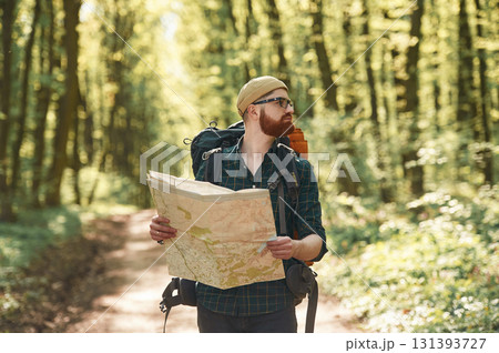 Focused on reading the map. Bearded man is in the forest at daytime Focused on reading the map. Bearded man is in the forest at daytime 131393727