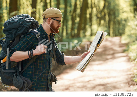 Focused on reading the map. Bearded man is in the forest at daytime 131393728