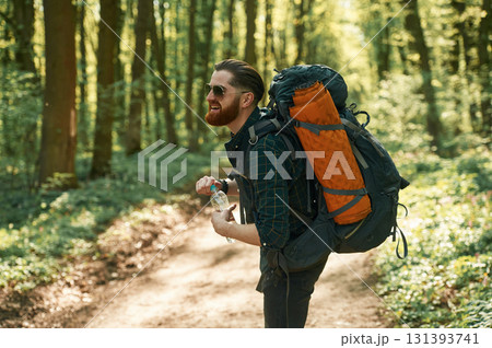 Bottle of water, holding. Bearded man is in the forest at daytime Bottle of water, holding. Bearded man is in the forest at daytime 131393741