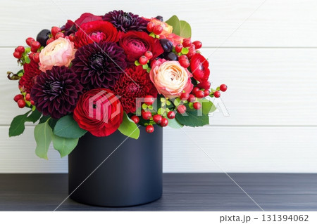 Lush red bouquet with roses, dahlias, and berries arranged in a black vase on a dark wooden table 131394062