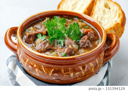 Hearty autumn soup garnished with parsley leaves and served with warm crusty bread in a rustic ceramic bowl 131394129