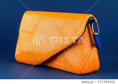 Bright orange clutch bag with bold asymmetrical lines stands out against a dramatic dark blue background showcasing modern design 131394202