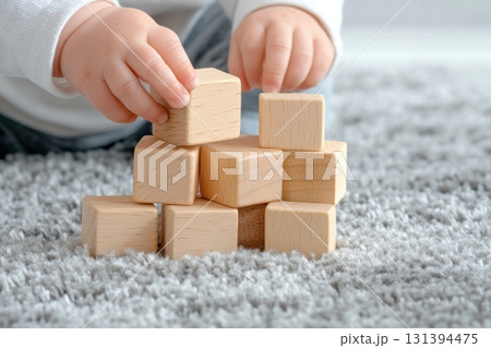 Toddler engages in creativity by stacking wooden blocks on a plush gray carpet under warm natural light Toddler engages in creativity by stacking wooden blocks on a plush gray carpet under warm natural light 131394475