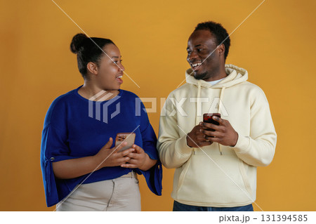 Using smartphones. Happy black couple are together against yellow background Using smartphones. Happy black couple are together against yellow background 131394585