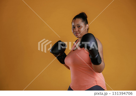Black boxing gloves, sports. African American woman is in the studio against yellow background 131394706