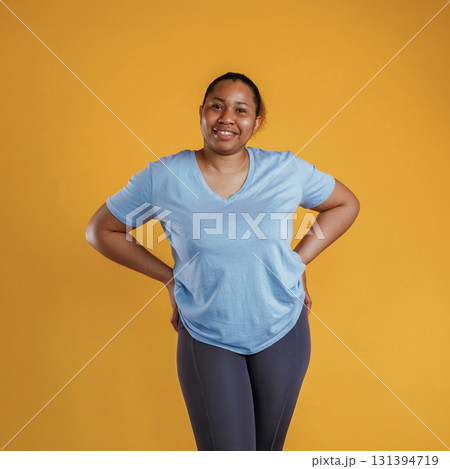 In blue shirt and black sportive leggings. African American woman is in the studio against yellow background 131394719