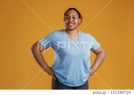 In blue shirt and black sportive leggings. African American woman is in the studio against yellow background In blue shirt and black sportive leggings. African American woman is in the studio against yellow background 131394720