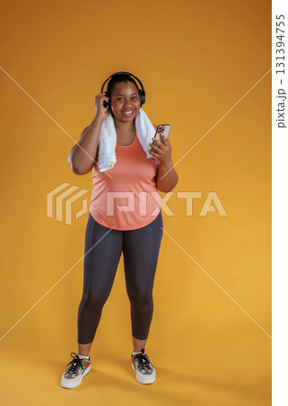 In headphones and with smartphone in hand. African American woman is in the studio against yellow background In headphones and with smartphone in hand. African American woman is in the studio against yellow background 131394755